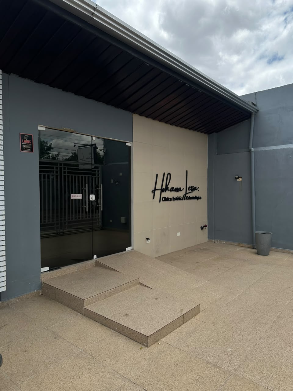 Entrada da clínica, com porta de vidro, rampa e o nome Hohana Lessa na parede